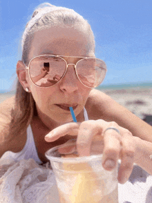 a woman wearing sunglasses drinks through a blue straw