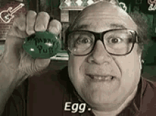 a man wearing glasses is holding a green egg that says `` egg '' .