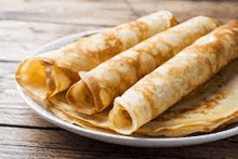 a white plate topped with three rolled pancakes on a wooden table .