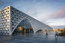 people walking in front of a large building with a geometric pattern