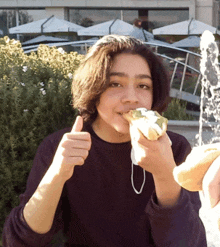 a young girl eating a sandwich and giving a thumbs up