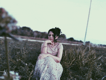 a woman in a lace dress sits in a grassy field