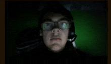 a man wearing glasses and a headset is looking at the camera in the dark .