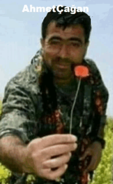 a man in a military uniform is holding a red flower and the name ahmet cagan is above him