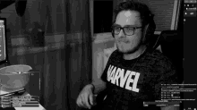 a man wearing glasses and a marvel shirt is sitting in front of a computer screen