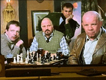 a group of men are sitting around a chess board .