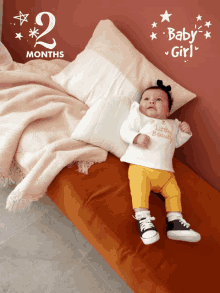 a baby girl is laying on a bed next to a pillow and a sign that says baby girl