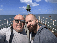 two men are posing for a picture on a pier