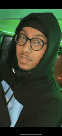 a man wearing glasses and a black hoodie is looking at the camera