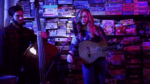 a woman is playing a guitar and a man is playing a double bass in front of a shelf filled with board games .