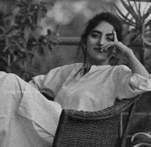 a woman in a white shirt sits in a chair with her hand on her face