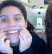 a woman is making a funny face in front of an apple computer monitor