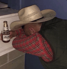 a man in a cowboy hat is holding a bottle of modelo