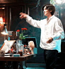 a man in a white shirt is standing in front of a desk with a vase of red roses on it