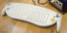 a keyboard that looks like a nintendo gamecube controller sits on a wooden floor