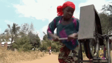 a woman in a red headband is playing a musical instrument on a dirt road with natgeotv.com on the bottom right