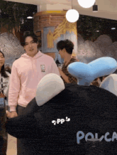 a man in a pink hoodie stands next to a stuffed animal that says pouca on it
