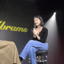 a woman sitting on a stool holding a microphone in front of a sign that says brans
