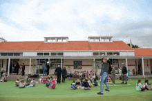 a group of children sit on the grass outside of a school