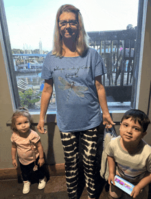 a woman wearing a blue shirt with a dragonfly on it stands in front of two children