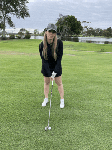 a woman holding a golf club on a golf course with a lake in the background