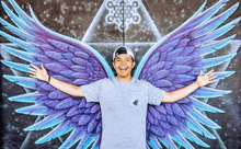 a man with purple and blue wings is standing in front of a painting of wings on a wall .