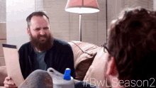 a man with a beard sits on a couch talking to another man with # bwl season 2 written on the bottom