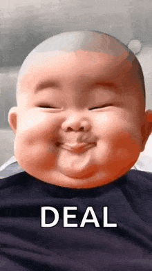 a baby with a bald head is smiling and making a funny face with the words `` deal '' behind him .