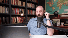 a man with a beard is sitting in front of a microphone with a map of the world behind him