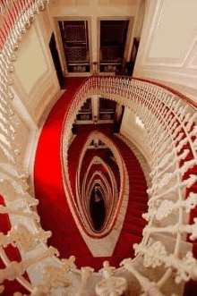 a spiral staircase with red carpet and white railing in a building .