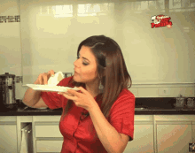 a woman in a red shirt is eating a piece of cake in a kitchen with a sign that says tapioca