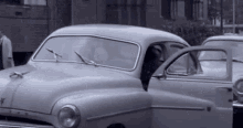 a black and white photo of a car with the door open and a man standing next to it .