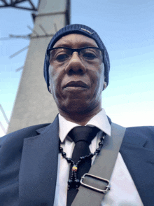 a man wearing a suit and a beanie has a necklace around his neck