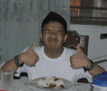 a young man giving a thumbs up while sitting at a table with a plate of food