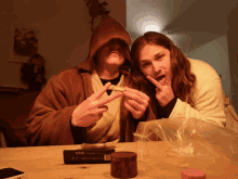 a man and a woman are sitting at a table with a box of ocb rolling papers