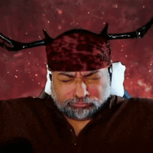 a man with a beard is wearing a red headband with horns on it
