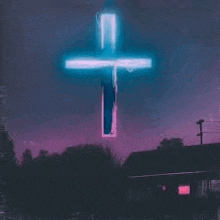 a neon cross is lit up in the night sky over a house .