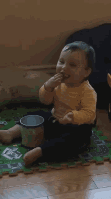 a baby is sitting on a puzzle mat with a cup in front of him that says ' milk ' on it