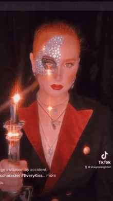 a woman with red hair and rhinestones on her face is holding a candle in her hand .