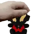 a hand is holding a black teddy bear with a red shirt on .