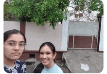 two girls pose for a picture in front of a fence