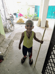 a young boy in a yellow tank top holds a cane