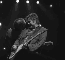 a man is kissing another man while playing a guitar on a stage in a black and white photo .