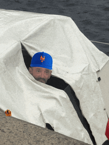 a man wearing a blue new york mets baseball cap is sticking his head out of a boat