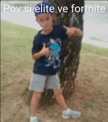 a young boy is standing next to a tree and giving a thumbs up sign