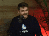 a man wearing a sweater that says cozy.tv stands in front of a microphone