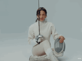a woman in a white sweater is holding a fencing sword