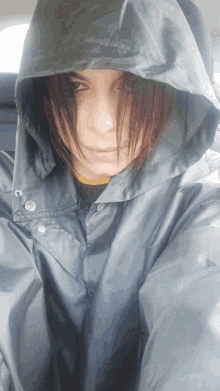 a woman wearing a black raincoat with a hood is taking a selfie