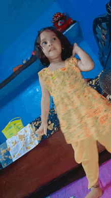 a little girl in a yellow dress stands in front of a blue wall with a bag that says ' apollo ' on it