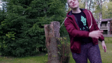 a man in a red jacket and a black shirt with a feather on it is standing in front of a tree stump